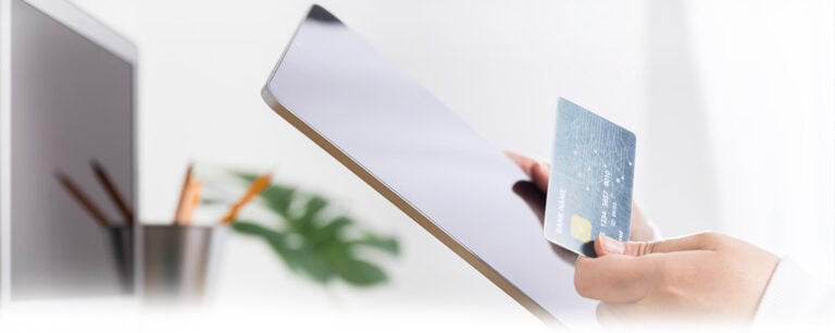 Person making an online payment using a credit card and tablet. AGMS secure payment processing solutions.